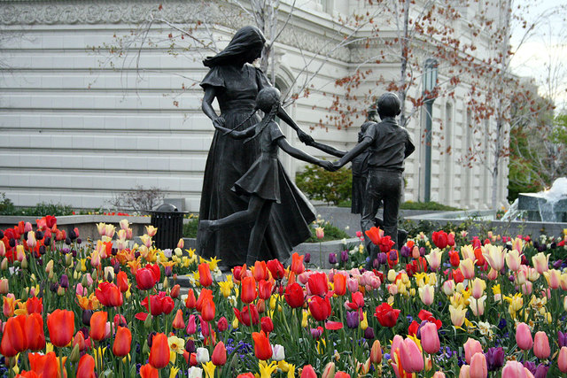 estátua da mulher com as crianças visto com muitas flores de cores diversas