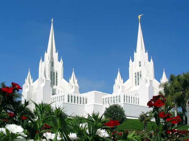 templo de cor branquíssimo, com vegetação e gramado verde com flores vermelhas