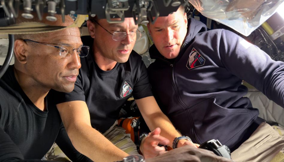 Astronautas Victor Glover, Reid Wiseman e Jeremy Hansen a borda da Artemis II configuram câmeras e equipamentos para a sobrevoo lunar.