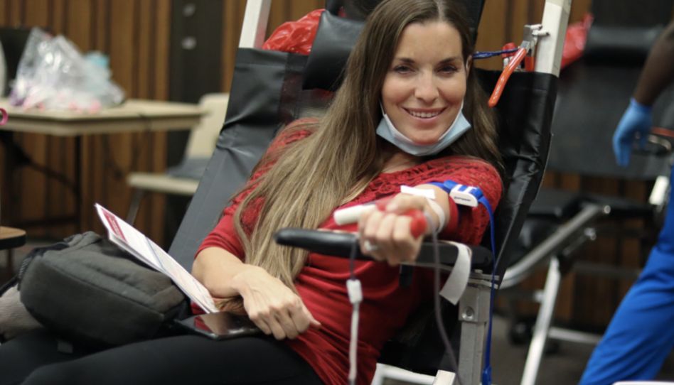 Mulher sorri para a câmera enquanto doa sangue.